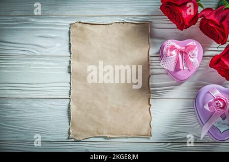 Heart-shaped metal present boxes red roses vintage paper on wooden board holidays concept. Stock Photo