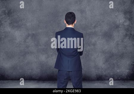 Facing the future with decisiveness. A rear view of a businessman standing and facing a blank wall. Stock Photo