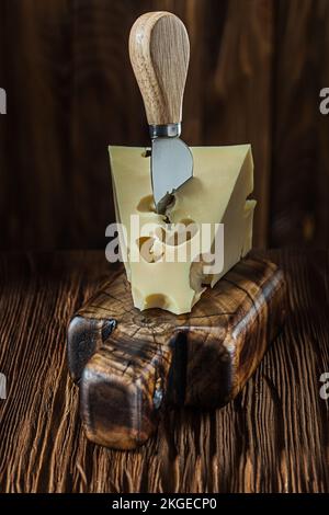 maasdam cheese on vintage cutting board and knife old dark wooden background Stock Photo