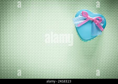 Metal blue heart-shaped gift box on green surface holidays concept. Stock Photo