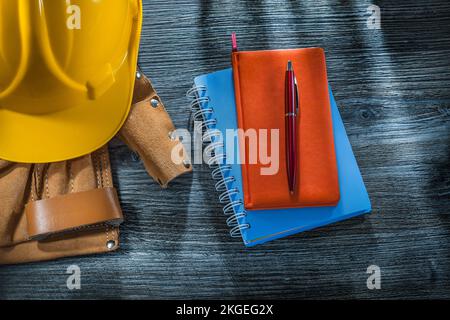 Notebooks pen building helmet tool belt on wooden board. Stock Photo