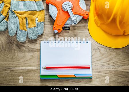 Notepad pencil protective gloves tape measure hard hat on wooden board. Stock Photo