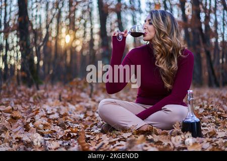 Beautiful plus size young indian woman enjoying a glass of red wine in the oak forest at sunset Stock Photo