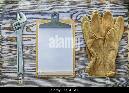 Protective gloves adjustable wrench clipboard on wooden board. Stock Photo