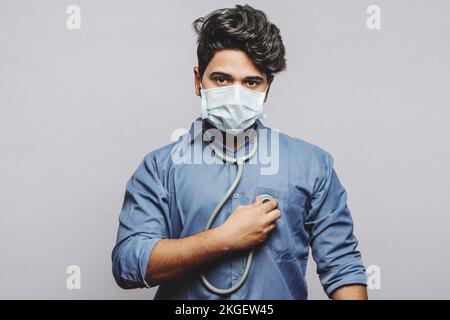A millennial doctor uses a stethoscope to listen to the beating of his own heart. A doctor examining his own heartbeat and looking at the camera. Stock Photo