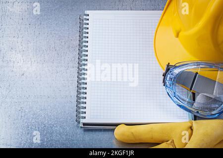 Safety glasses gloves copybook building helmet on scratched metallic background. Stock Photo