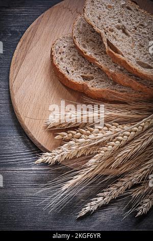 Sliced bread on wooden chopping board bunch of wheat rye ears directly above. Stock Photo