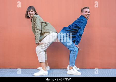 Two happy excited stylish diverse gen z woman and man friends dancing and having fun, trendy outfits people  dancing together isolated on pink wall ba Stock Photo