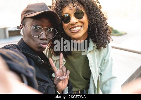 two young african american women taking selfie, hip hop street style, friends using app mobile to connect to social media, positive image and gesture Stock Photo