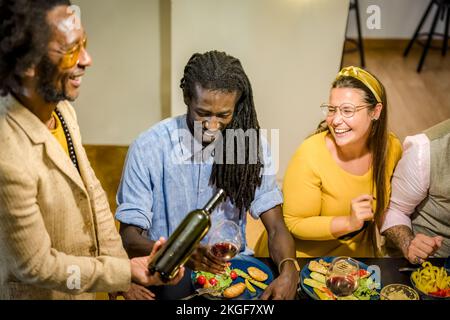 Happy vegan friends eating and drinking, deverse people smiling and laughing at vegetarian party, mutli age and multiracial group Stock Photo