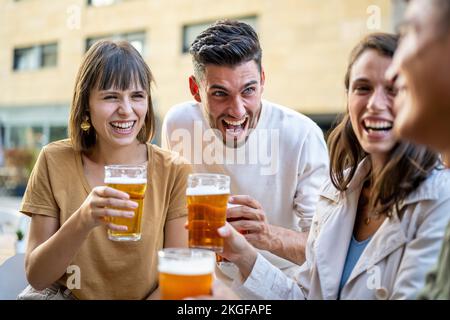 Group of friends drinking beers and laughing, generation z people at pub having fun and toasting with beerglasses, young couples enjoying time togethe Stock Photo