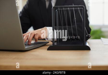 Businessman working on laptop computer at his office desk with Newton's pendulum Stock Photo