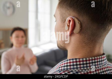 Deaf young man wearing hearing device on his ear communicating with other people Stock Photo