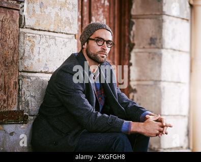 Thoughts sink deeper than words. a handsome young man seated next to a sidewalk in the city while being in deep thought. Stock Photo