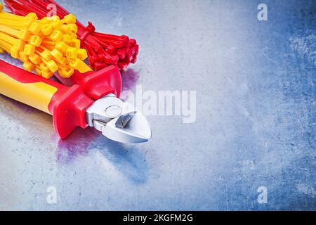 Wire cutter tying cables on scratched metallic background. Stock Photo
