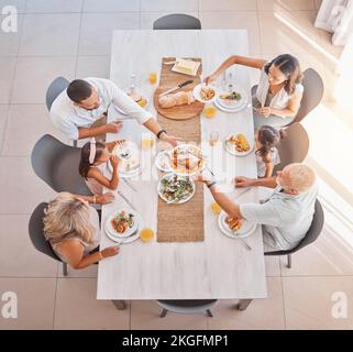 Family, lunch and food at the table with big family bonding, sharing and eating together at the dining table. Meal, top view and family home with a Stock Photo