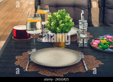 Empty plate, fork and knife on table. Green flowers. Water in glasses. Stock Photo