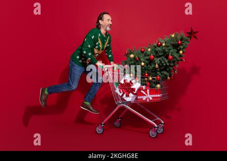 Full size profile portrait of overjoyed cheerful man jumping push market trolley isolated on red color background Stock Photo