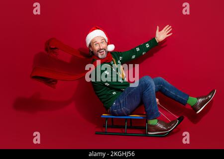 Full size profile portrait of overjoyed positive person sit ride sledge flying scarf isolated on red color background Stock Photo
