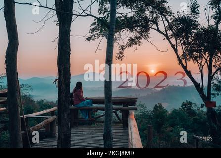 2023 Happy New Year, Young woman sitting on the nature beautiful sunrise mountain landscape view to celebrate new year coming. Stock Photo