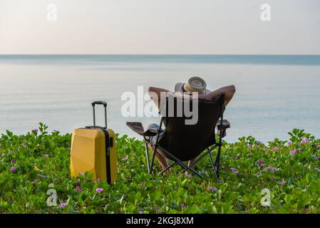 Man sitting on the chair beside suitcase at the beach, vacation, relaxing time concept. Stock Photo