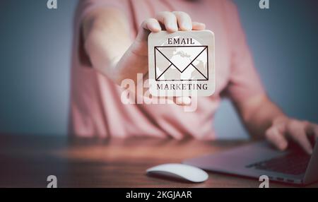 Email marketing concept, Man using Laptop computer and  holding wooden plate  with Email icon and writing Email Marketing text. Stock Photo