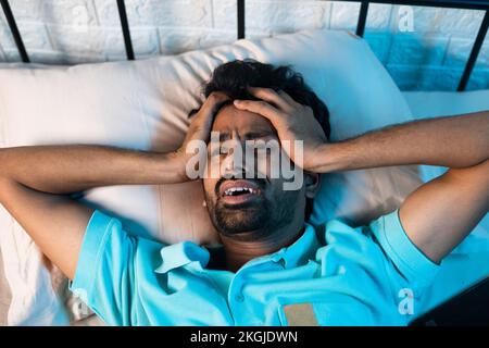 screaming young man suffering from sleeplessness or insomnia disorder at night on bedroom - concept of drug addict, migraine and stress Stock Photo