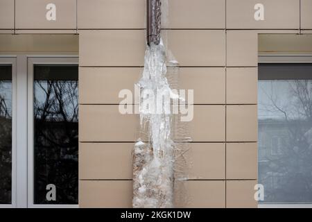 Frozen rain pipe on an apartment building. Ice on the building wall. Stock Photo