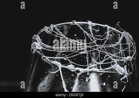 A closeup shot of glue stick strings on a glass with water droplets on a dark background Stock Photo