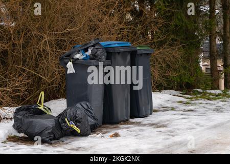 Garbage bin full of trash on white snow in residential area in winter. Stock Photo