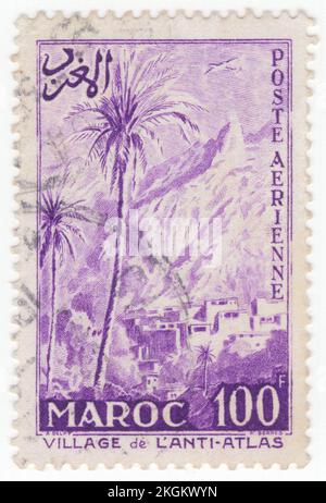 FRENCH MOROCCO - 1955 July 25: An 100 franc bright violet Air Post stamp depicting Airplane over Village in the Anti-Atlas, also known as Lesser Atlas or Little Atlas, is a mountain range in Morocco, a part of the Atlas Mountains in the northwest of Africa. The Anti-Atlas extends from the Atlantic Ocean in the southwest toward the northeast, to the heights of Ouarzazate and further east to the city of Tafilalt, altogether a distance of approximately 500 km. The range borders on the Sahara to the south Stock Photo