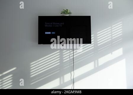 Large screen television on a bedroom wall with cord hanging down with shadows from window blinds Stock Photo