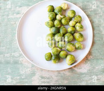 Cooked Brussels sprouts on a white plate isolated on wooden background. Closeup and flat lay Stock Photo