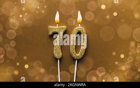 Burning golden glitter number 70 celebration candle on brown bokeh background Stock Photo