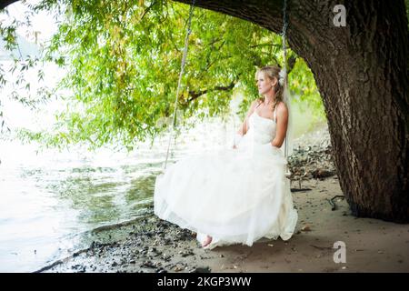 Germany, Rhineland-Palatinate, portrait of pensive bride sitting on a swing at waterside of Rhine river Stock Photo