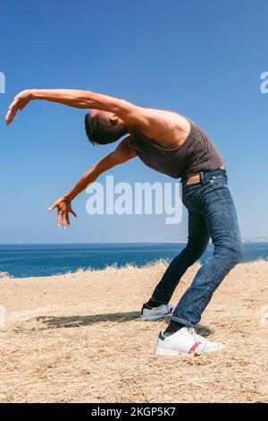 Man dancing on field in front of sea on sunny day Stock Photo