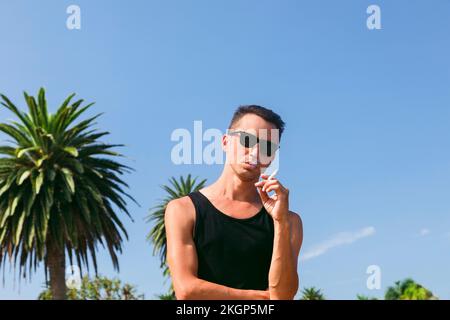 Man with cigarette standing in front of blue sky Stock Photo