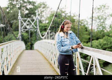 Teenage girl using smartphone and listening music on a bridge Stock Photo