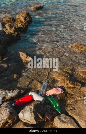 Empty plastic bottles and slippers floating on water at beach Stock Photo