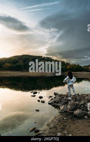 Astronaut holding space helmet standing on rock at beach Stock Photo