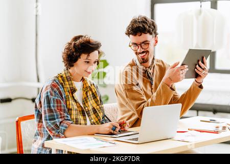 Happy illustrator with colleague using graphics tablet and laptop at desk Stock Photo