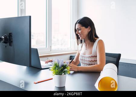 Smiling young architect working on laptop in office Stock Photo