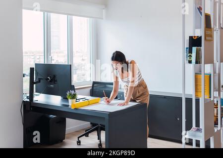 Young architect leaning on desk analyzing blueprint in office Stock Photo