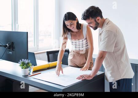 Young architect with colleague discussing blueprint in office Stock Photo