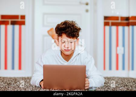 Smiling boy lying on carpet in front of laptop at home Stock Photo