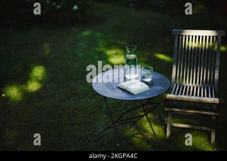 Open book and glass of water on table with chair in garden Stock Photo