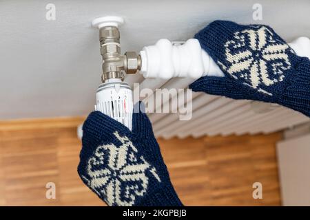 Hands of senior man wearing woolen gloves adjusting temperature of radiator Stock Photo