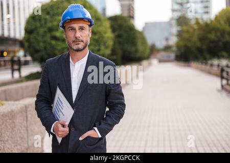 Contemplative engineer wearing hardhat standing at footpath Stock Photo