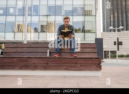 Man sitting on bench and reading book Stock Photo