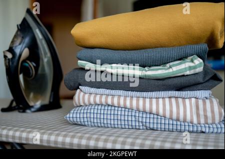 Iron by stack of clean clothes on ironing board at home Stock Photo